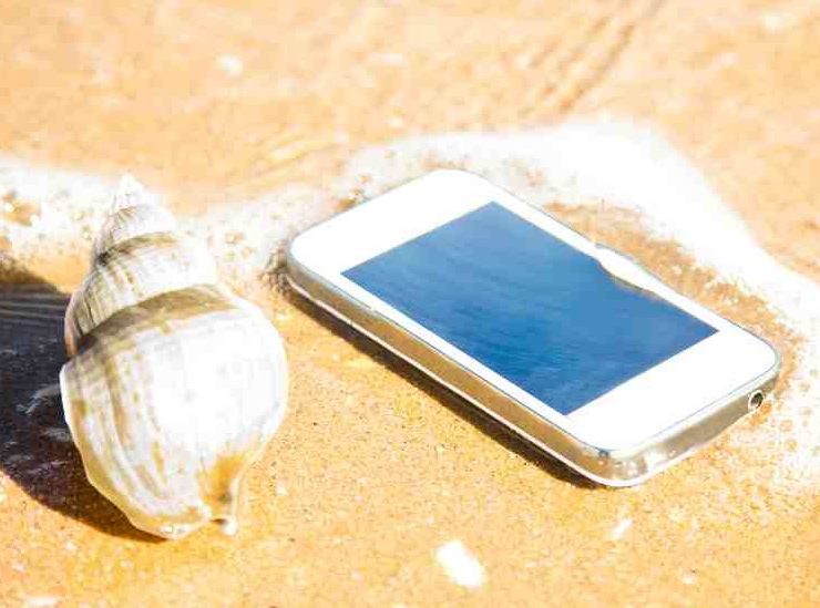 Smartphone in mare sulla spiaggia accanto a una conchiglia